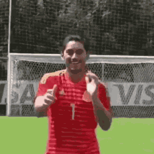 a man in a red and yellow striped shirt is standing in front of a soccer goal on a field .