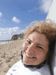 a woman leaning against a wall on the beach smiling