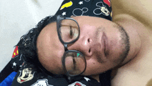 a man wearing glasses and a mickey mouse hat is sleeping on a bed