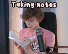 a young man in a pink shirt is taking notes