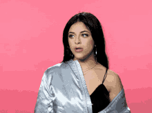 a woman wearing hoop earrings and a white jacket is standing in front of a pink background