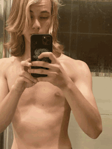 a shirtless man takes a selfie with his phone