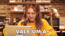 a girl in a yellow hoodie looks at a tablet and says vale um a +