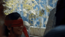 a woman wearing a red blindfold is smiling in front of a window