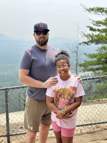 a man wearing a red sox hat stands next to a little girl