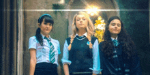 three girls in school uniforms are standing next to each other in a room .