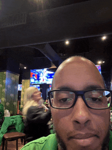 a man wearing glasses and a green shirt takes a selfie in a restaurant