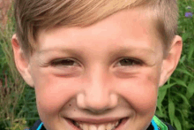 a young boy is smiling for the camera while standing in front of some plants .