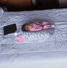 a baby is laying on a bed next to a laptop