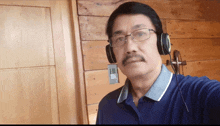 a man wearing glasses and headphones takes a selfie in front of a wooden wall