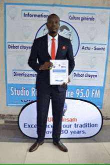 a man in a suit and tie is holding a certificate in front of a sign that says studio rire 95.0 fm