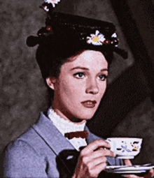 a woman in a hat is holding a cup of tea .