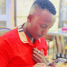 a man in a red shirt with a lion on it looks at his phone