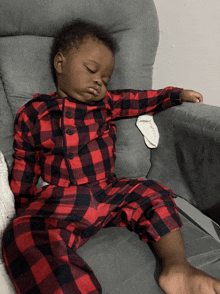 a baby in a red and black plaid outfit sleeping in a chair