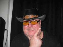 a man wearing a cowboy hat and sunglasses holds his finger to his face