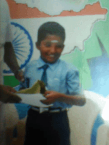 a young boy in a blue shirt and tie is smiling and holding a piece of paper