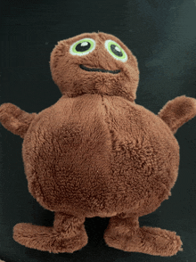 a brown stuffed animal with big green eyes is sitting on a black surface