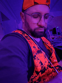 a man wearing glasses and an orange vest with a purple background