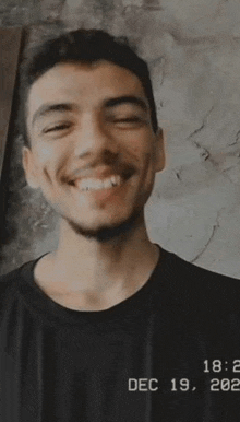 a young man with a beard is smiling while wearing a black t-shirt .