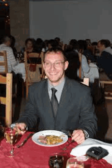 a man in a suit and tie is sitting at a table eating a meal .