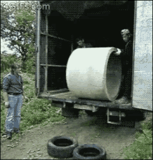 a man is standing in front of a truck that has a large concrete pipe in the back of it