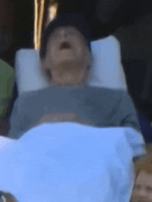 a man is laying in a hospital bed with his mouth open and his eyes closed .