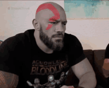 a bald man with a beard is wearing a bloodline shirt