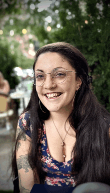 a woman wearing glasses and a tattoo on her arm smiles