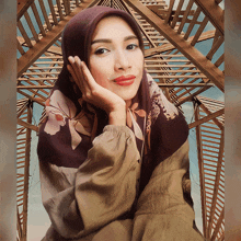 a woman wearing a floral scarf and a hijab stands in front of a wooden structure