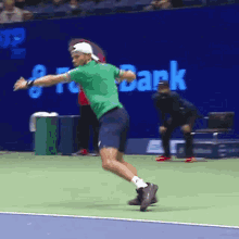 a man in a green shirt is jumping in the air on a tennis court in front of a sign that says bank