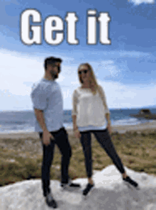 a man and a woman are standing next to each other on top of a hill near the ocean .