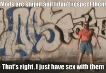 a man standing in front of a wall with graffiti on it that says mods are stupid