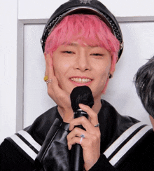 a young man with pink hair holds a microphone and smiles