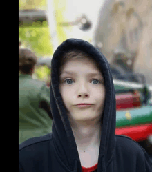 a young boy wearing a black hoodie looks at the camera with a blurry background