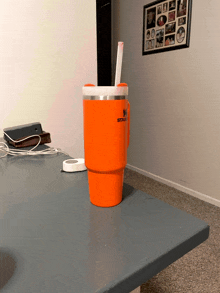 an orange stanley tumbler with a straw in it sits on a table