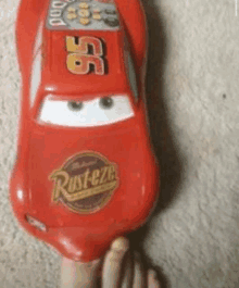 a person is holding a toy lightning mcqueen car on their foot .