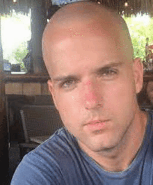 a bald man wearing a blue shirt is taking a selfie in a restaurant .