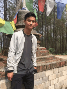 a young man stands in front of a brick wall with flags hanging from it