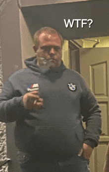 a man wearing a bmw sweatshirt is smoking a cigarette in front of a door