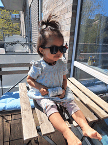 a little girl wearing sunglasses is sitting on a bench