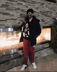 a man wearing a face mask holds a dog in front of a fire place