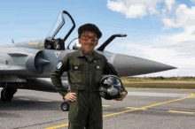 a man in a military uniform holds a helmet in front of a jet