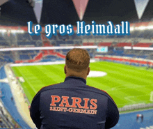 a man wearing a paris saint-germain jacket stands in front of a stadium