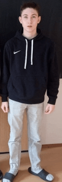 a young man is wearing a black nike hoodie and gray pants .