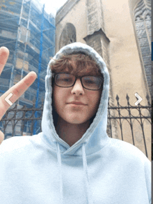 a young man wearing glasses and a light blue hoodie shows a peace sign