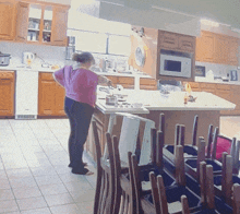 a woman in a pink shirt is standing in a kitchen with a stack of chairs in front of her