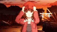 a girl wearing a red hat and a red jacket is standing in front of a sunset .