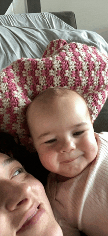 a baby is laying on a woman 's lap with a pink and white blanket on her head