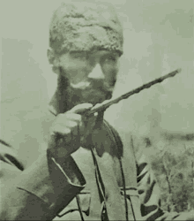 a black and white photo of a man with a beard holding a stick .