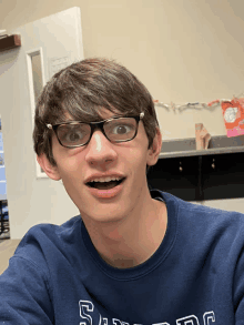 a young man wearing glasses and a blue shirt that says ' s.f.d.c. ' on it